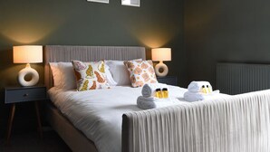 Una cama bien hecha con almohadas, una mesita de noche con lámpara y una obra de arte en la pared.