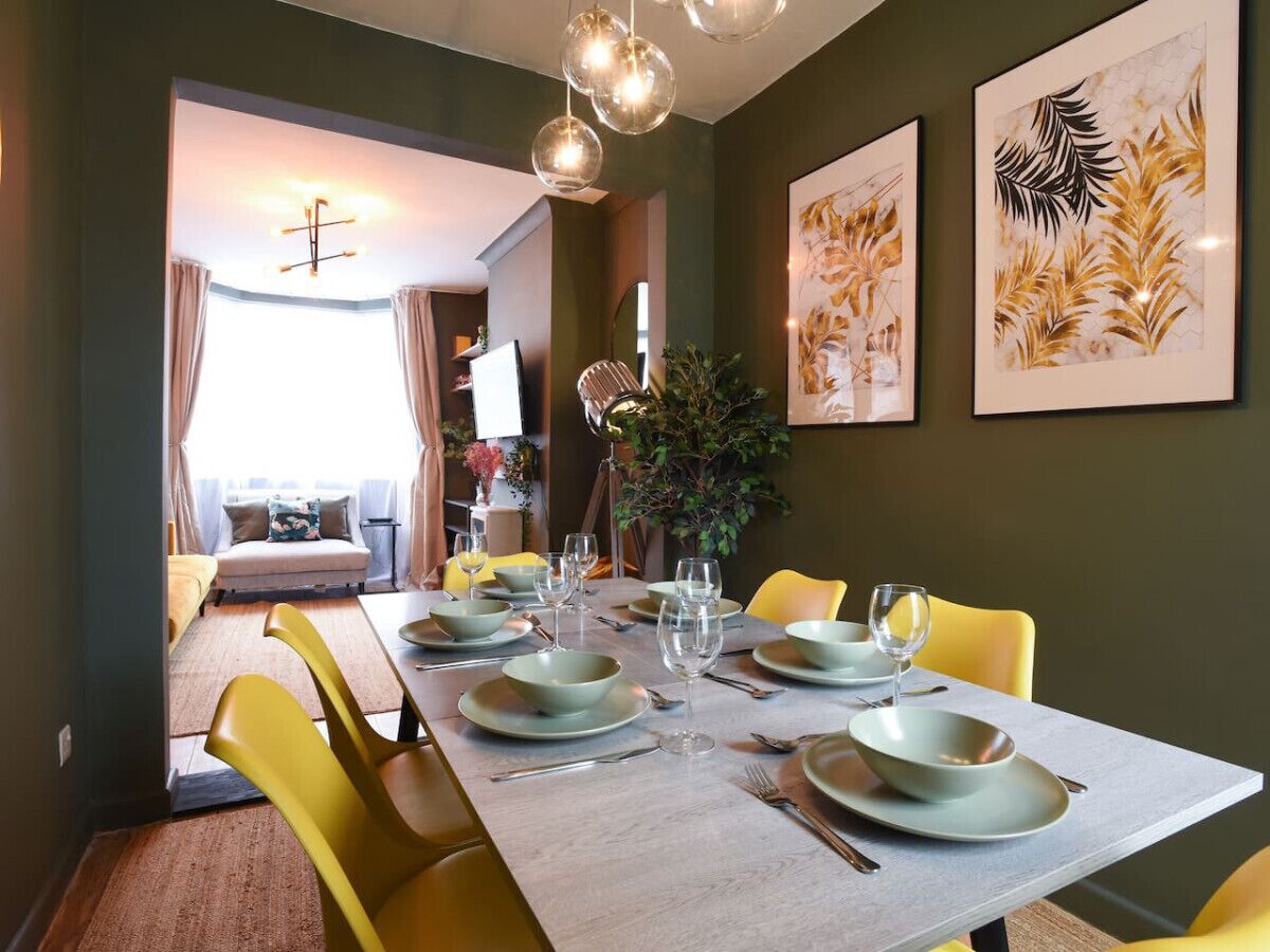 A dining area with a long table set for six, yellow chairs, and framed artwork on the walls.