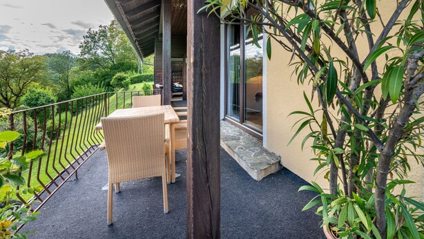 A balcony with wicker furniture, a stone pathway, and a view of the surrounding greenery. - Zeitlos by Interhome (Reifnitz)