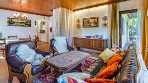 A cozy living room with wooden ceiling, leather sofas, a dining table, and a view of greenery outside. - Zeitlos by Interhome (Reifnitz)