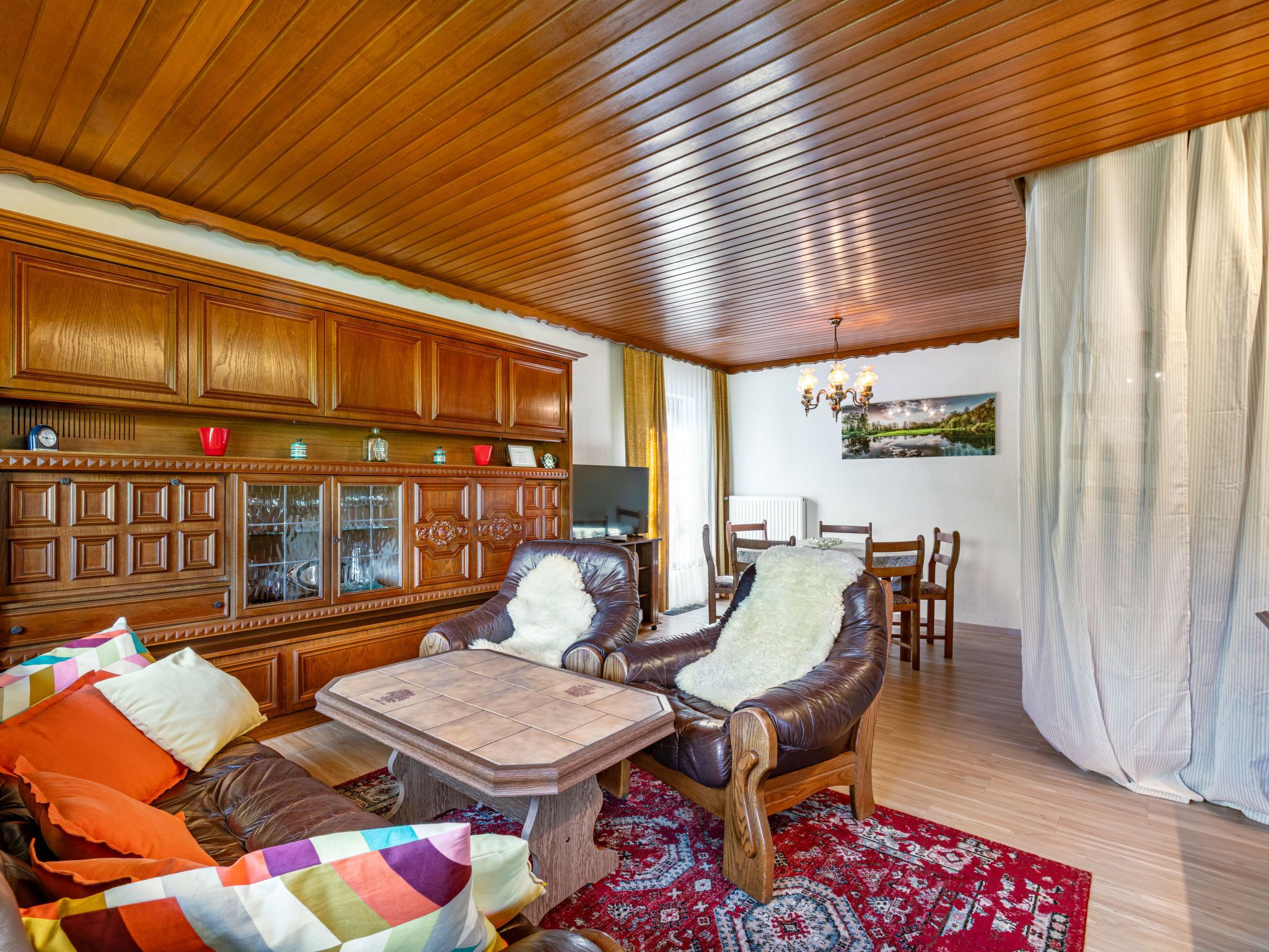 Un salón amplio con paneles de madera, un sofá de cuero, una mesa de comedor y una alfombra roja estampada.