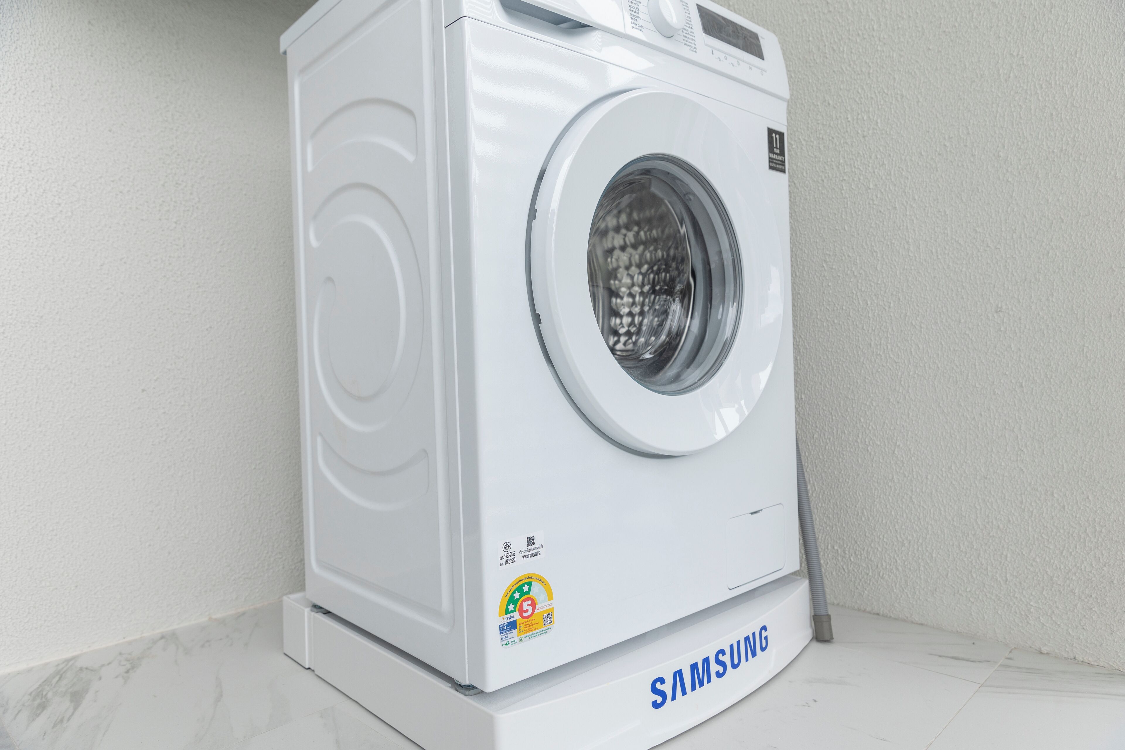 Une machine à laver Samsung blanche, placée dans un coin, sur un sol en marbre.