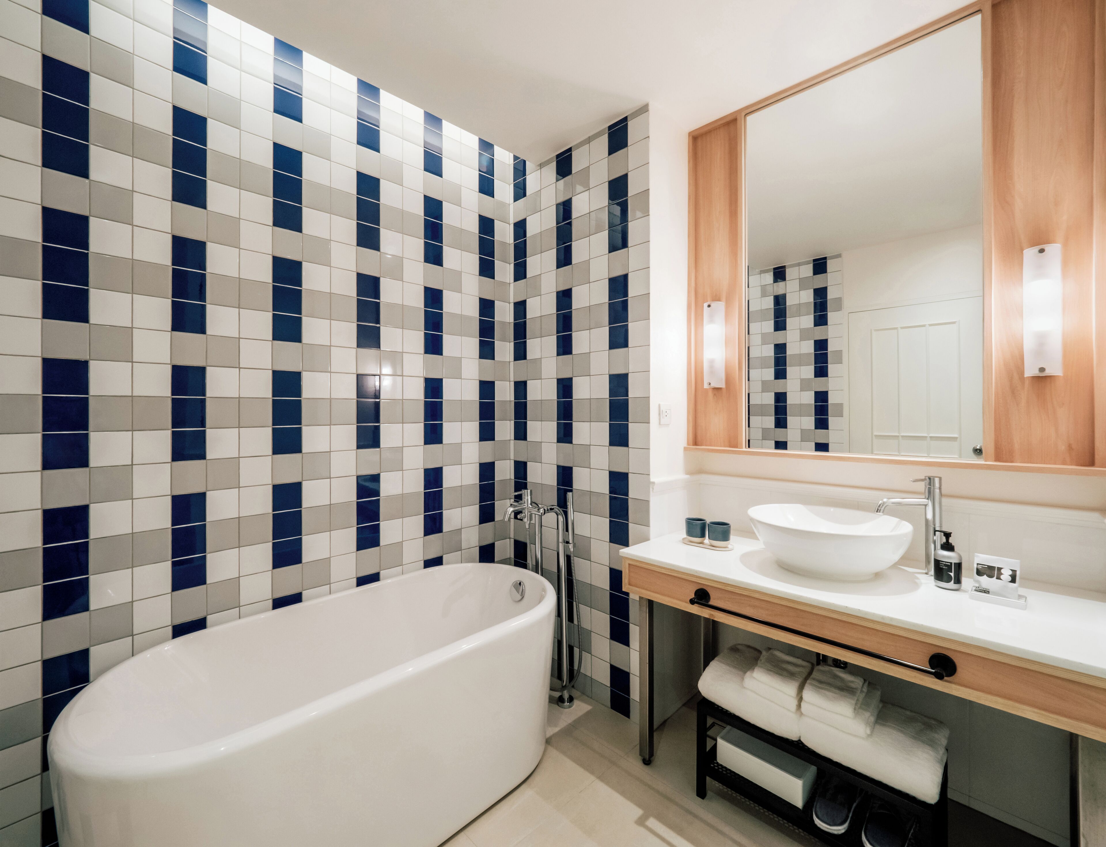 Un baño moderno con una bañera independiente, un lavabo con espejo y una pared de azulejos con un estampado azul y blanco.