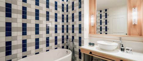 Un baño moderno con una bañera independiente, un lavabo con espejo y una pared de azulejos con un estampado azul y blanco.
