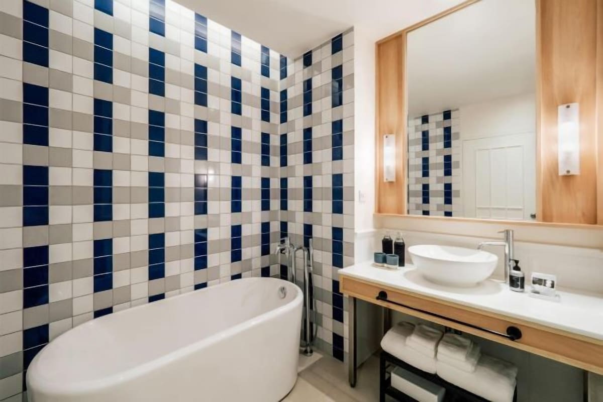 Une salle de bain avec un mur recouvert de carreaux à motifs, une baignoire sur pieds, un lavabo avec un miroir au-dessus et un porte-serviettes.