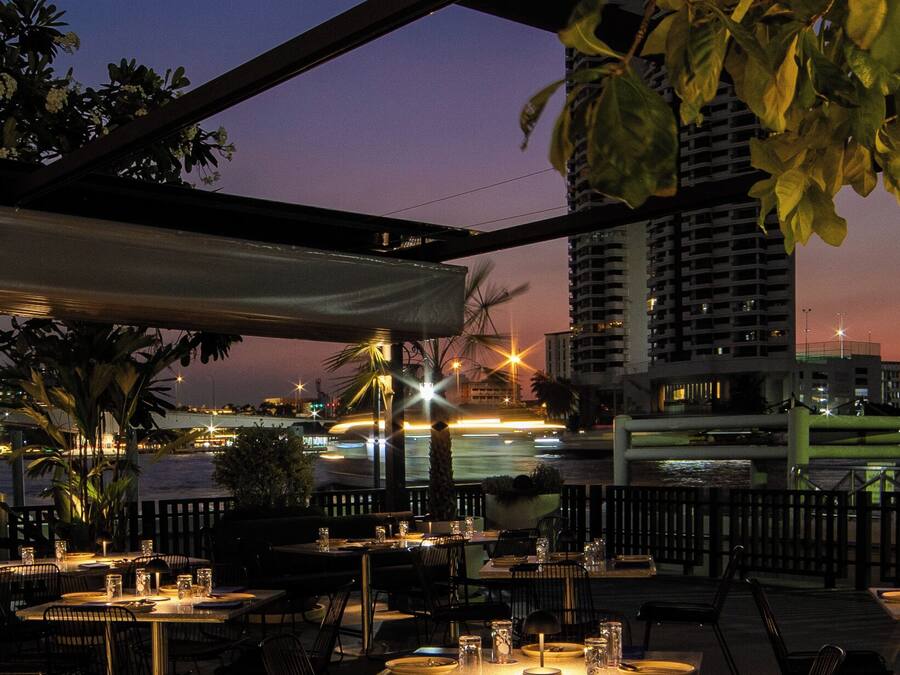 An outdoor dining area with tables and chairs, a view of a cityscape at dusk, and a building in the background.