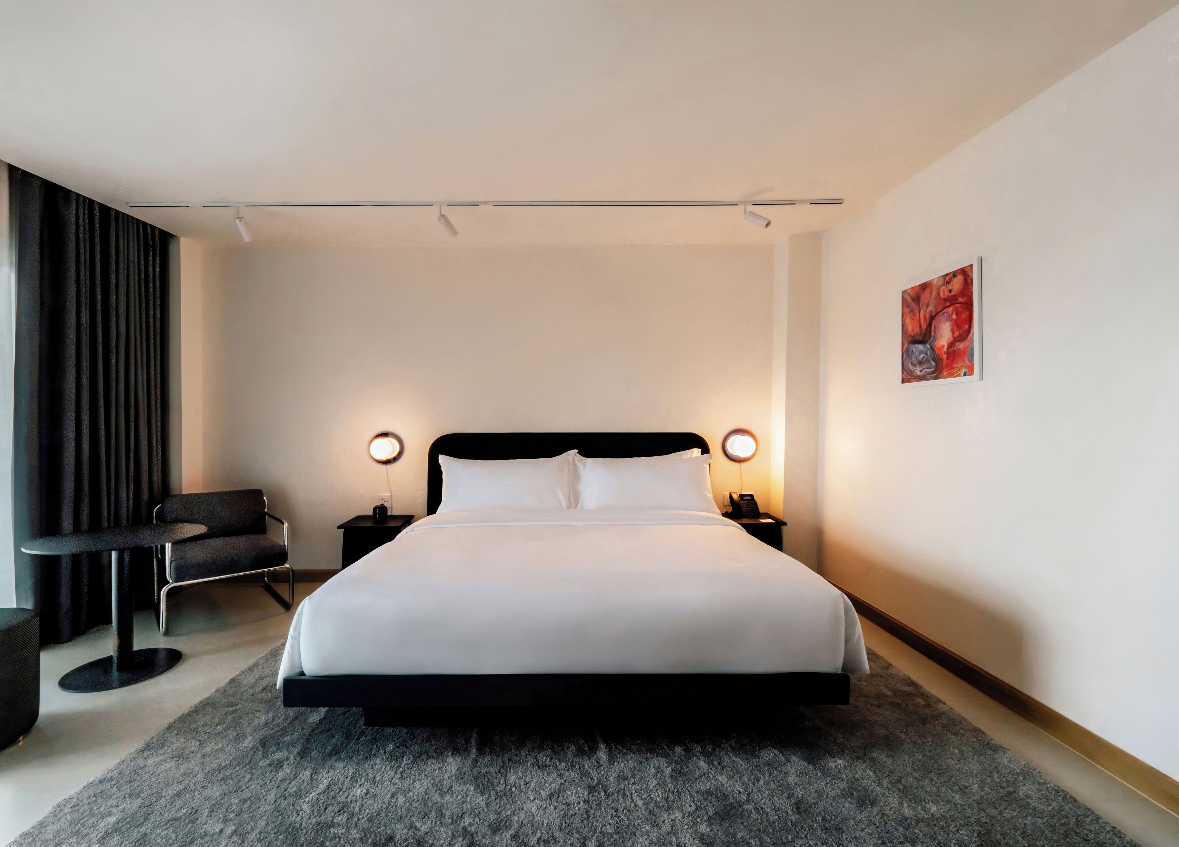 Una habitación de hotel moderna con una cama grande, lámparas de noche, una mesita pequeña y una silla.