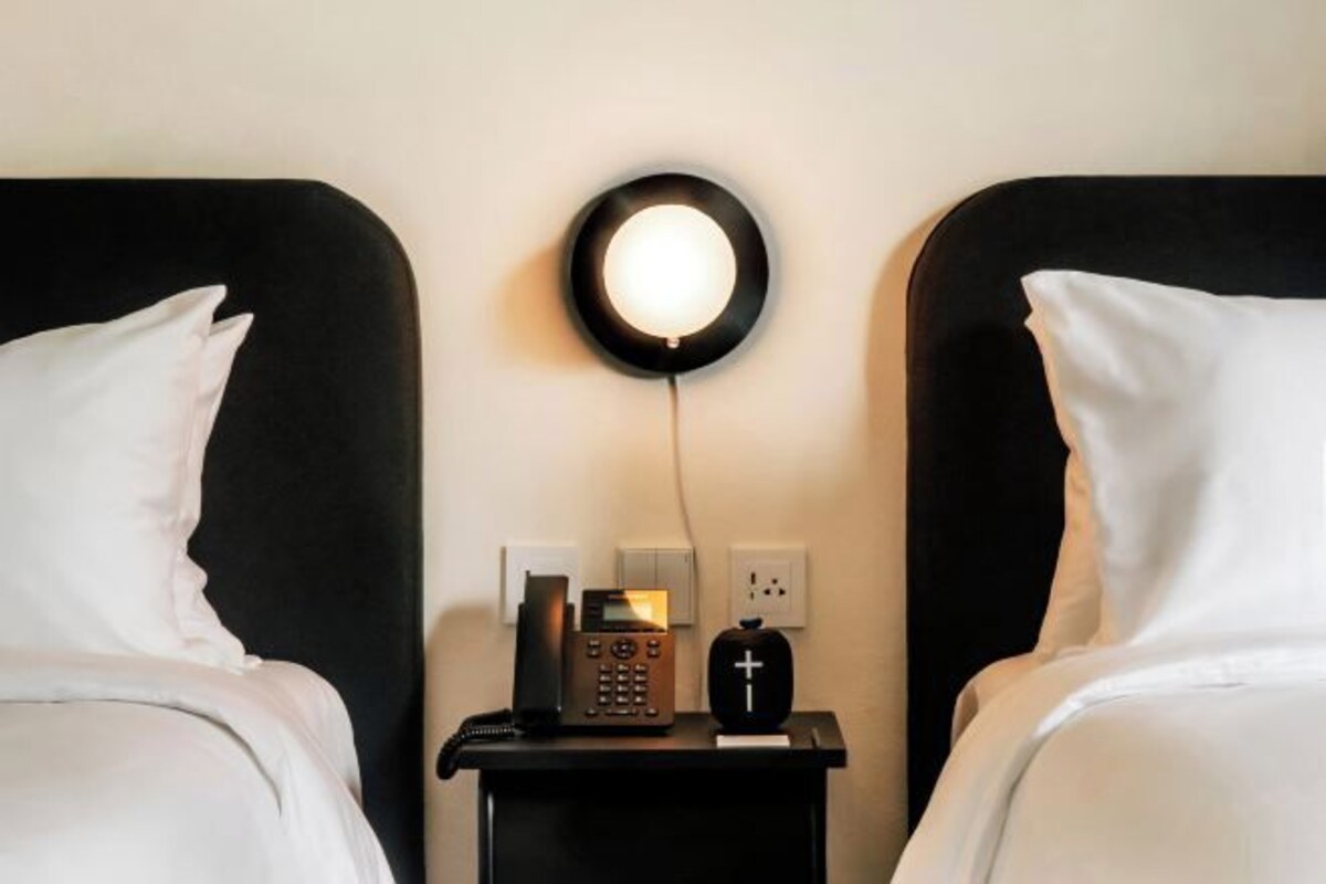 Een hotelkamer met twee bedden, een nachtkastje met een telefoon, een lamp en een wandlamp.