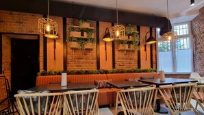 Un restaurant chaleureux aux murs de briques, agrémenté de luminaires suspendus et doté d’un espace détente avec des bancs rembourrés et des chaises en bois.