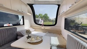 Un intérieur chaleureux avec un canapé, une petite table sur laquelle sont posées des tasses et une assiette, et une fenêtre donnant sur l’extérieur.