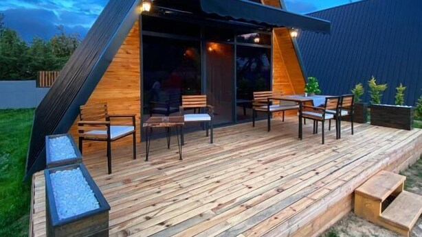 Un bâtiment moderne de forme triangulaire, doté d’une terrasse en bois et d’un espace extérieur aménagé pour s’asseoir.