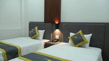 Une chambre d’hôtel avec deux lits, chacun doté d’une tête de lit grise et de linge de lit blanc. On y trouve une table de chevet avec une lampe et un téléphone. La chambre présente un design moderne, avec un mur d’accent en bois.