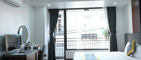 A hotel room with a bed, a desk, a TV, and a large window with curtains.