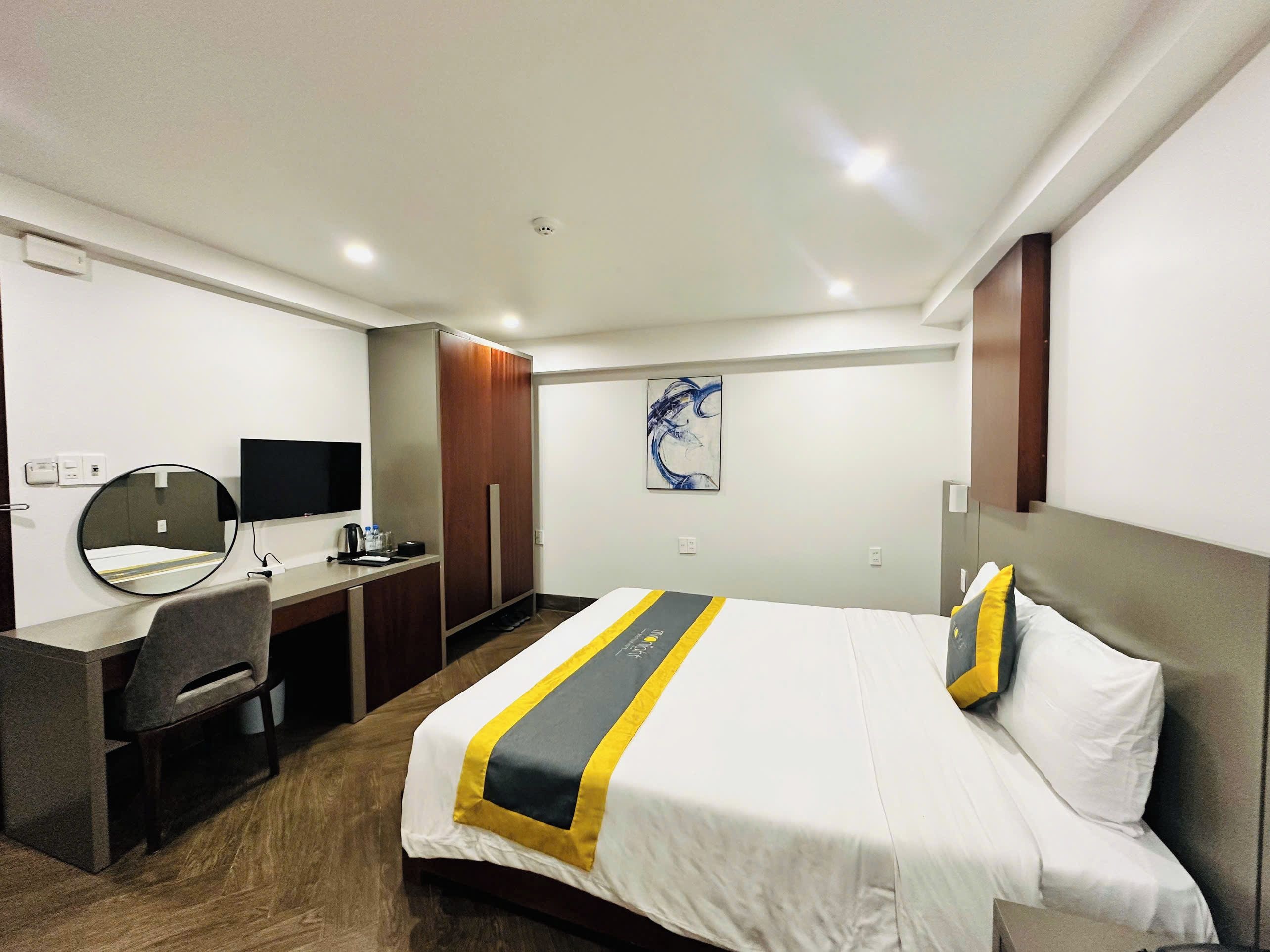 A hotel room with a bed, a desk, a chair, a television, and a wall-mounted artwork.