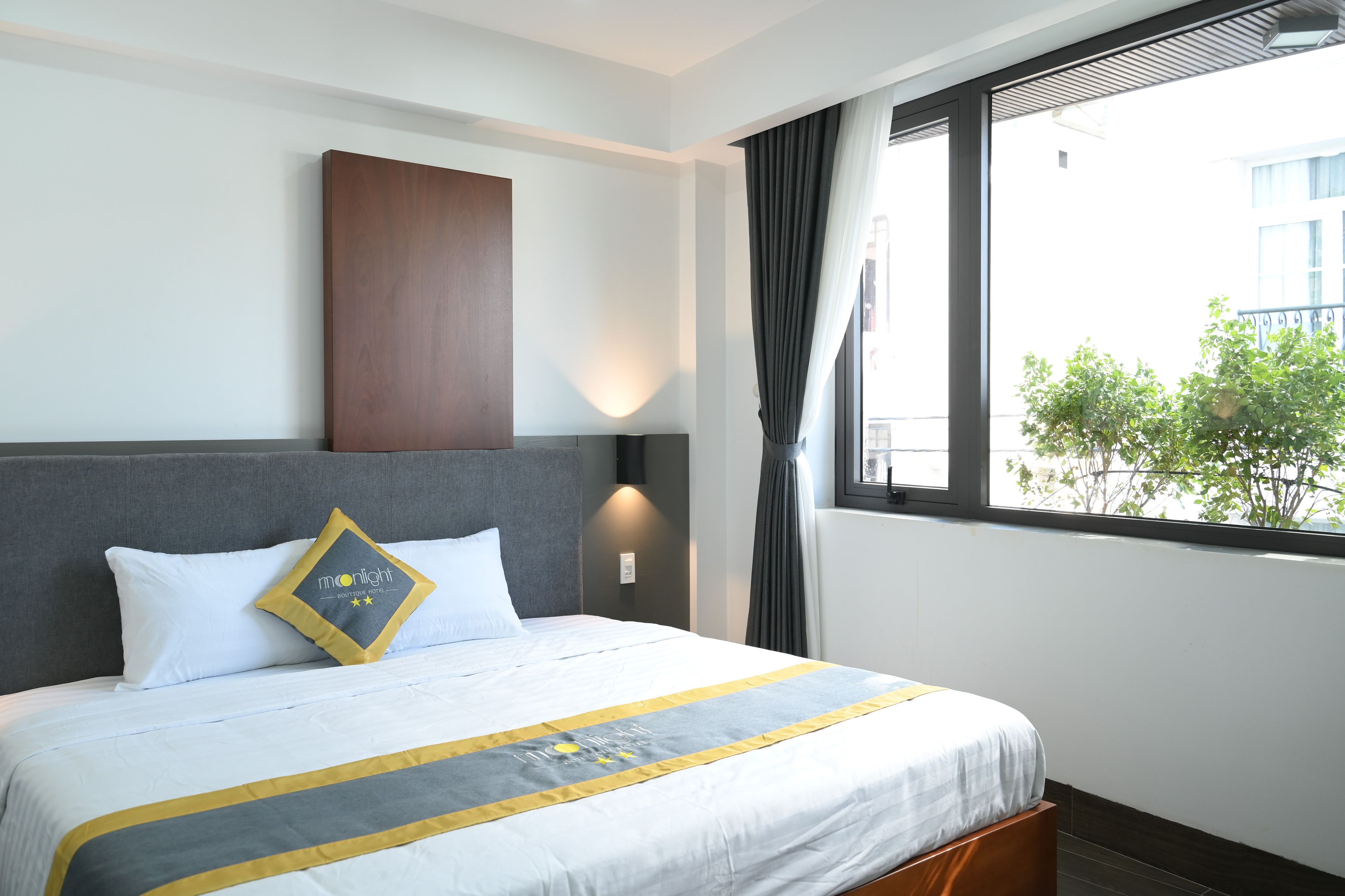 Une chambre d’hôtel avec un lit, une table de chevet, une lampe fixée au mur et une fenêtre avec des rideaux.