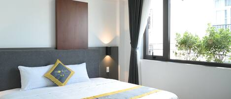 Una camera d'albergo con un letto, un comodino, una lampada a parete e una finestra con tende.