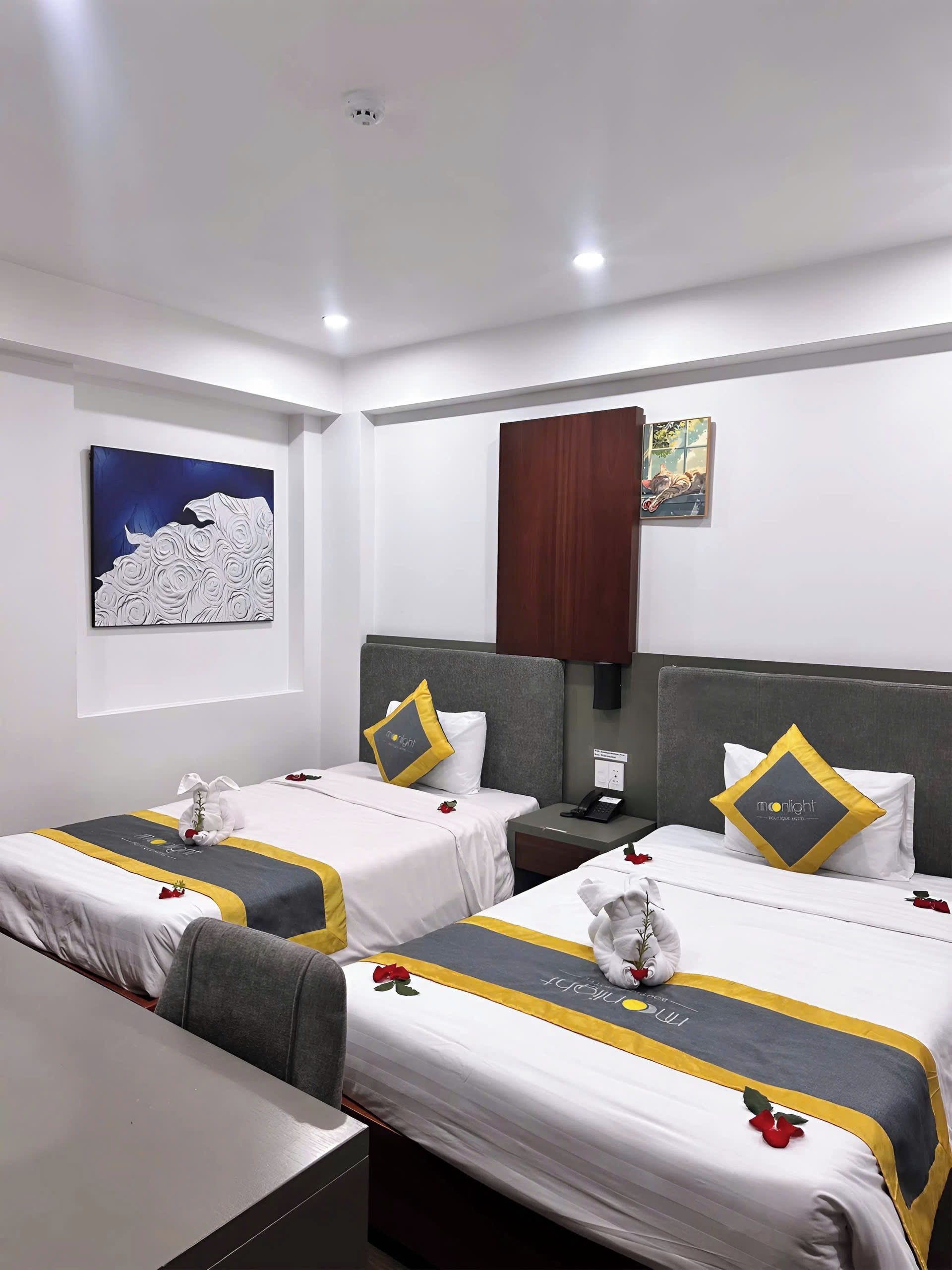 A hotel room with two beds, a painting on the wall, a wooden cabinet, and a nightstand with a phone.