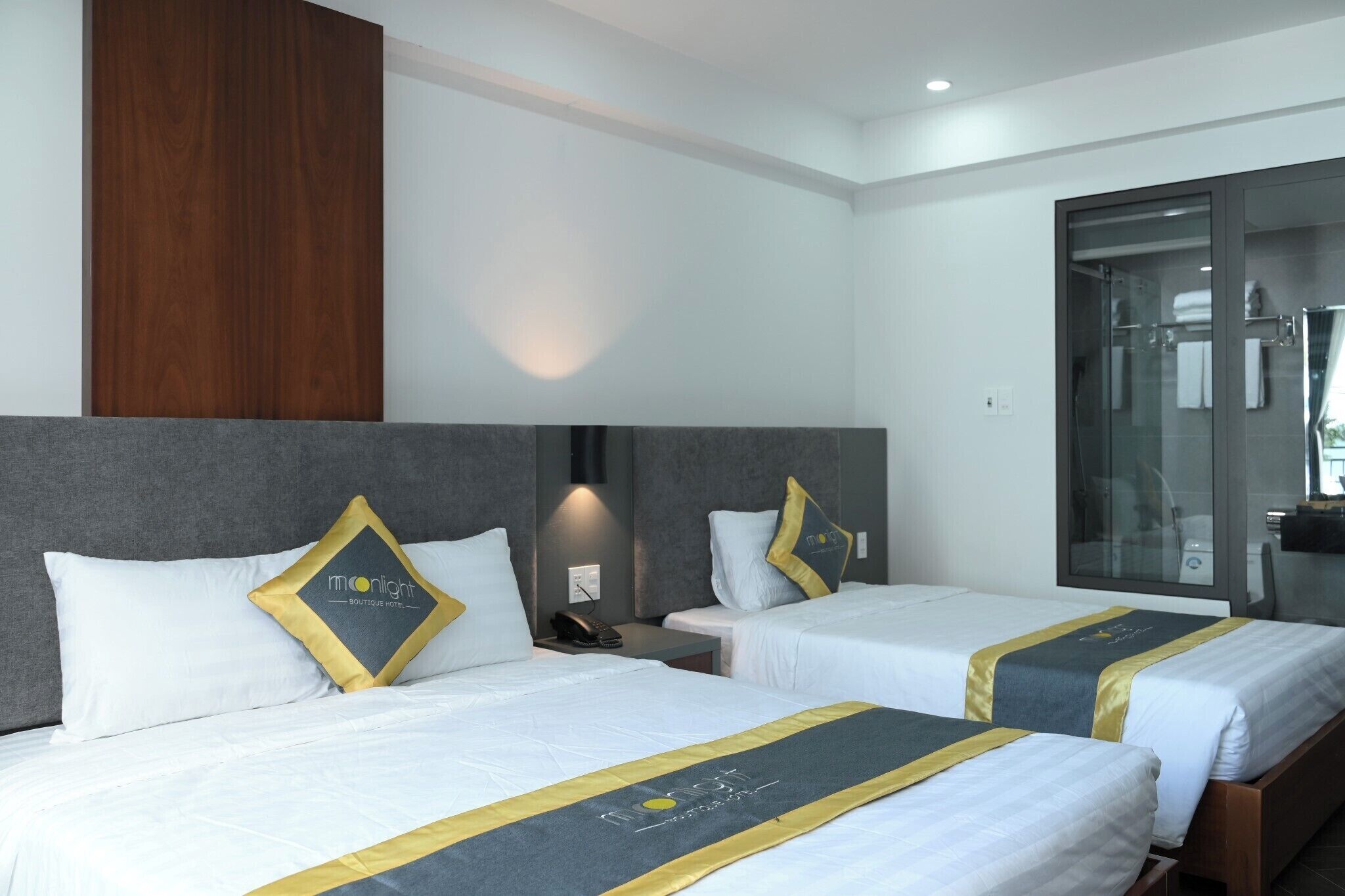 Habitación de hotel con dos camas, un panel de pared de madera, una mampara de ducha de vidrio y una mesita de noche con teléfono.