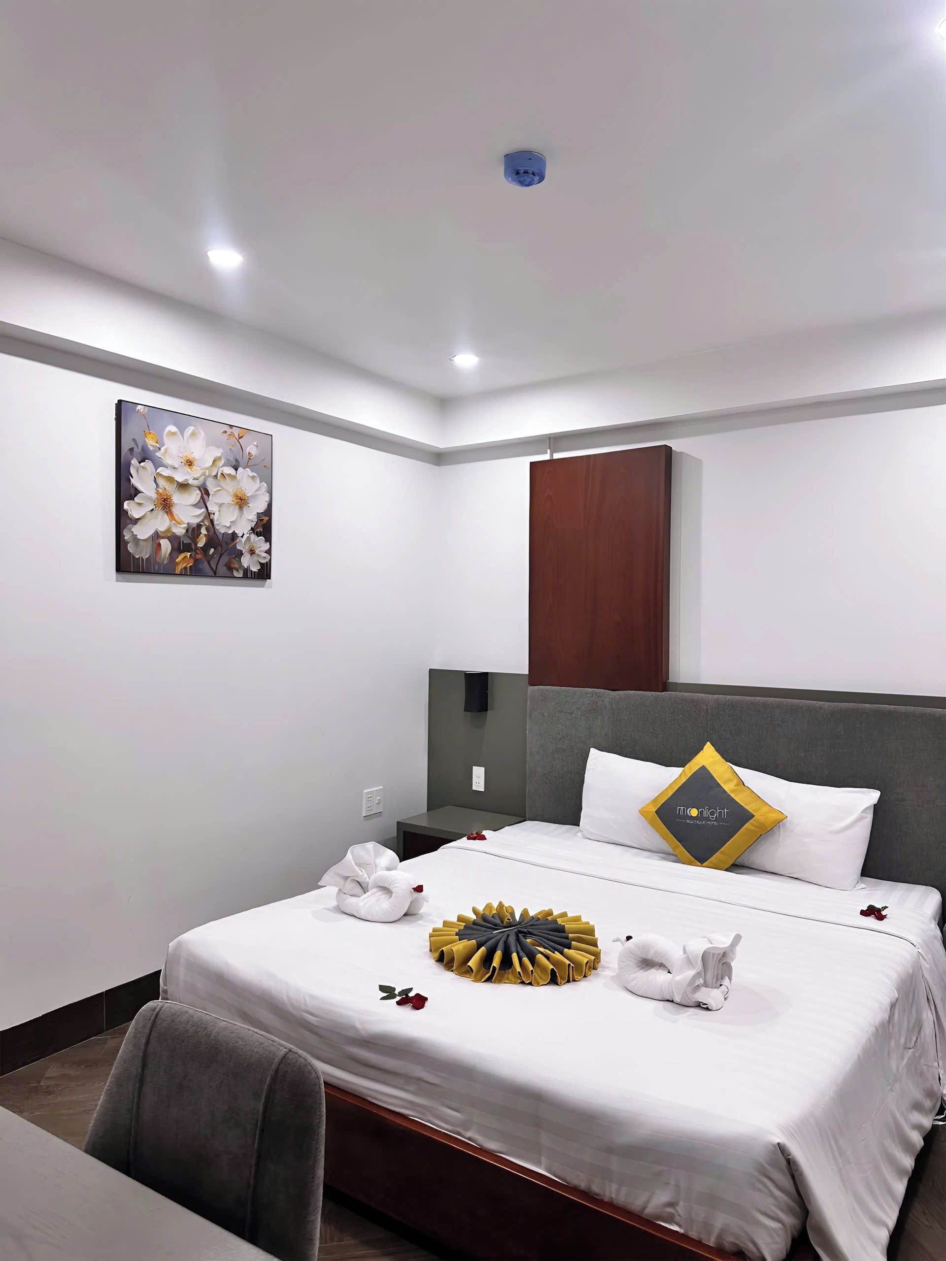 A hotel room with a bed, a painting, a nightstand, and a chair.