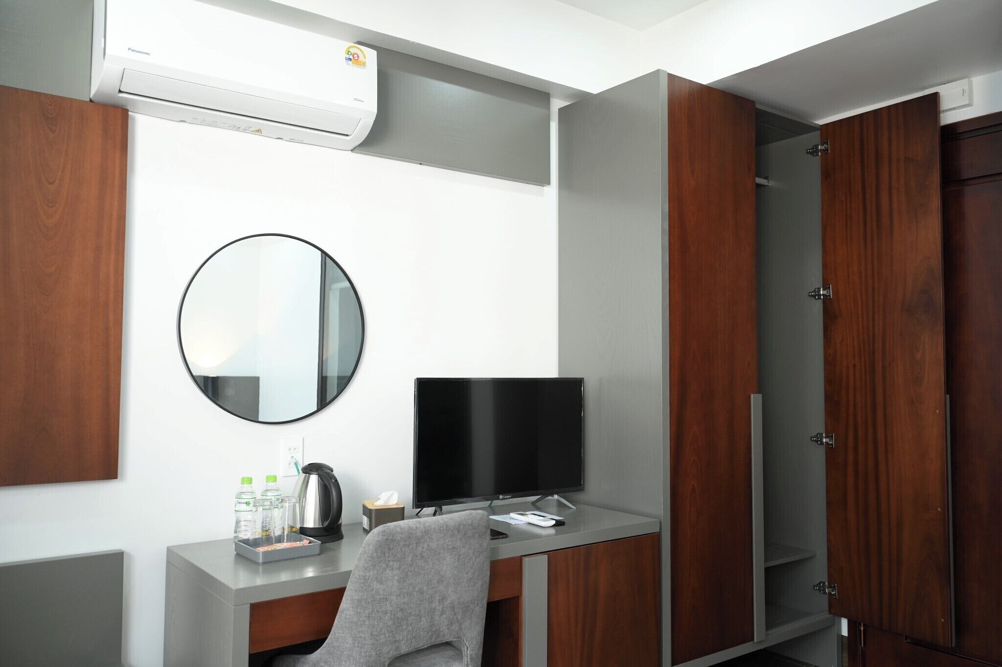 Una habitación de hotel moderna con escritorio, televisión de pantalla plana, espejo redondo y armario.