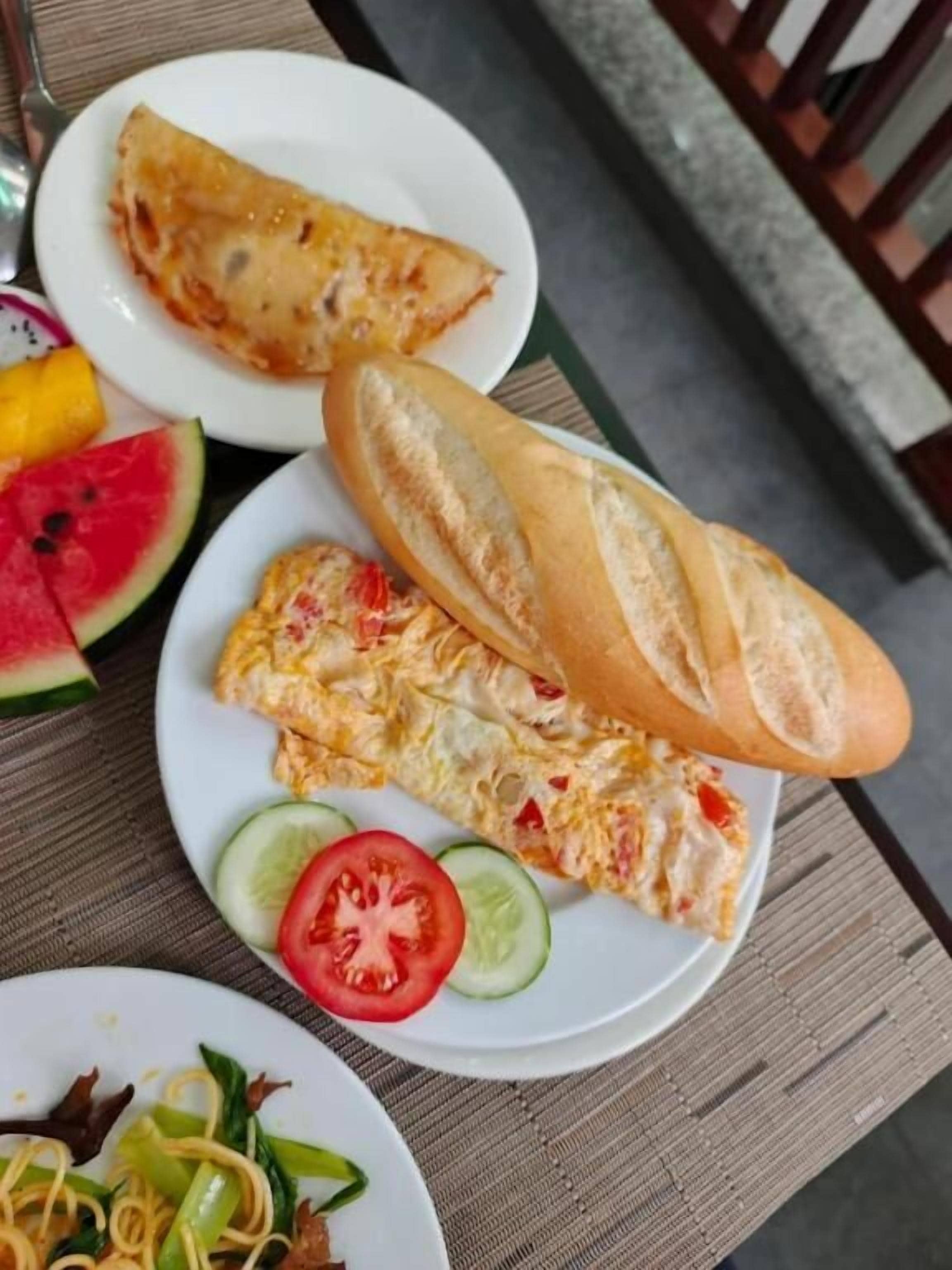 Une table avec des assiettes de nourriture, notamment un sandwich, une part d’omelette et une assiette de légumes.