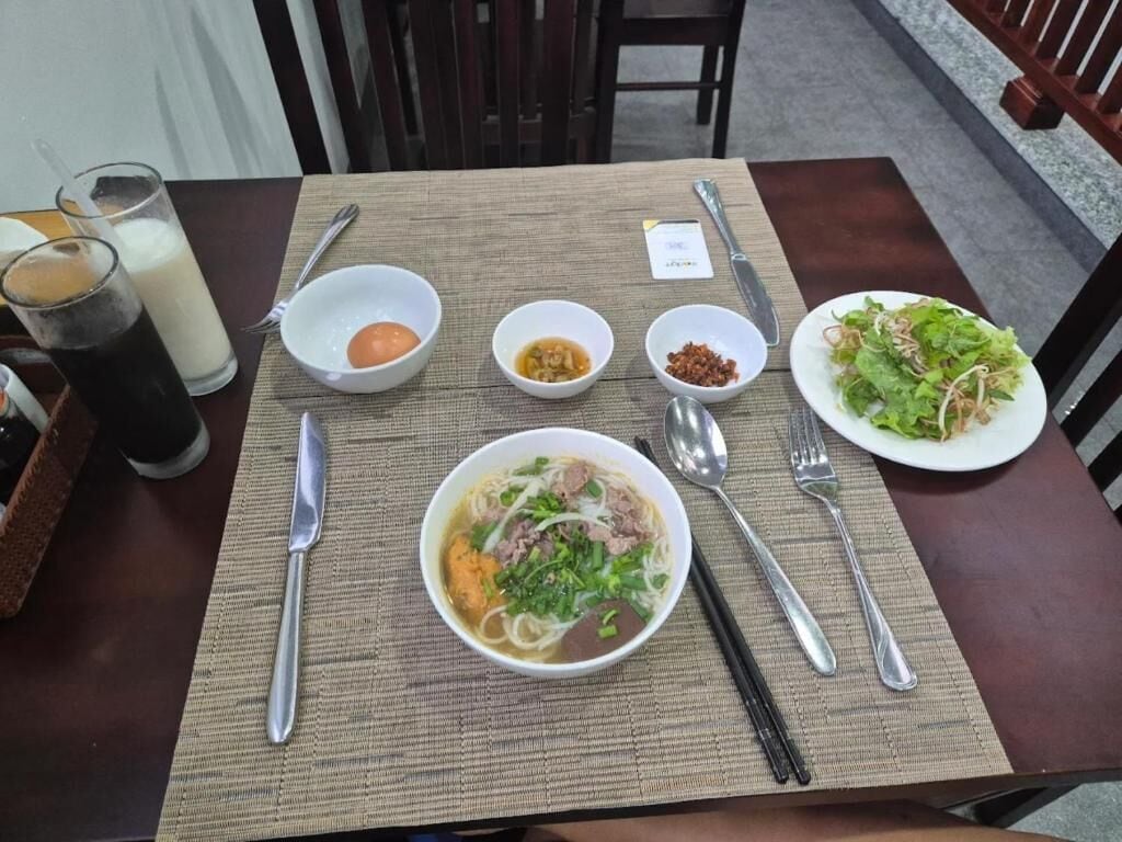 Una mesa servida con un tazón de sopa de fideos, una ensalada y dos vasos de una bebida oscura.