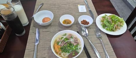 A table set with a bowl of noodle soup, a plate of salad, and two glasses of a dark beverage.