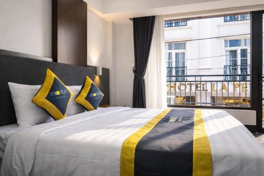 A hotel room with a large bed, two pillows, a nightstand, a window with curtains, and a view of the hotel exterior.