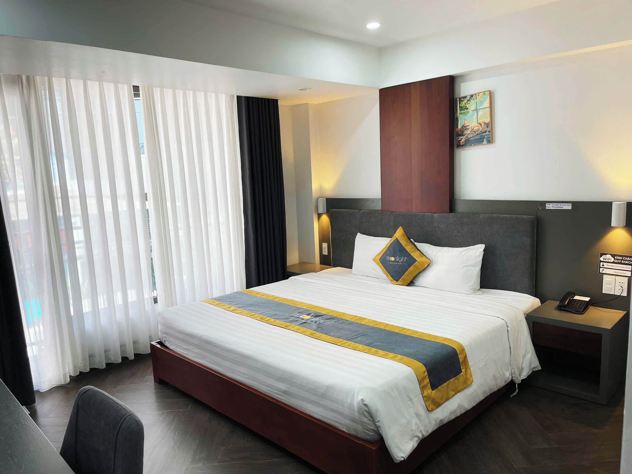 Habitación de hotel con una cama grande, un escritorio y una silla. Hay una ventana con cortinas, un cuadro en la pared y un cartel que indica disponibilidad de WiFi.