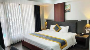 Une chambre d’hôtel avec un grand lit, un bureau et une chaise. Il y a une fenêtre avec des rideaux, un tableau au mur et un panneau indiquant la disponibilité du Wi-Fi.