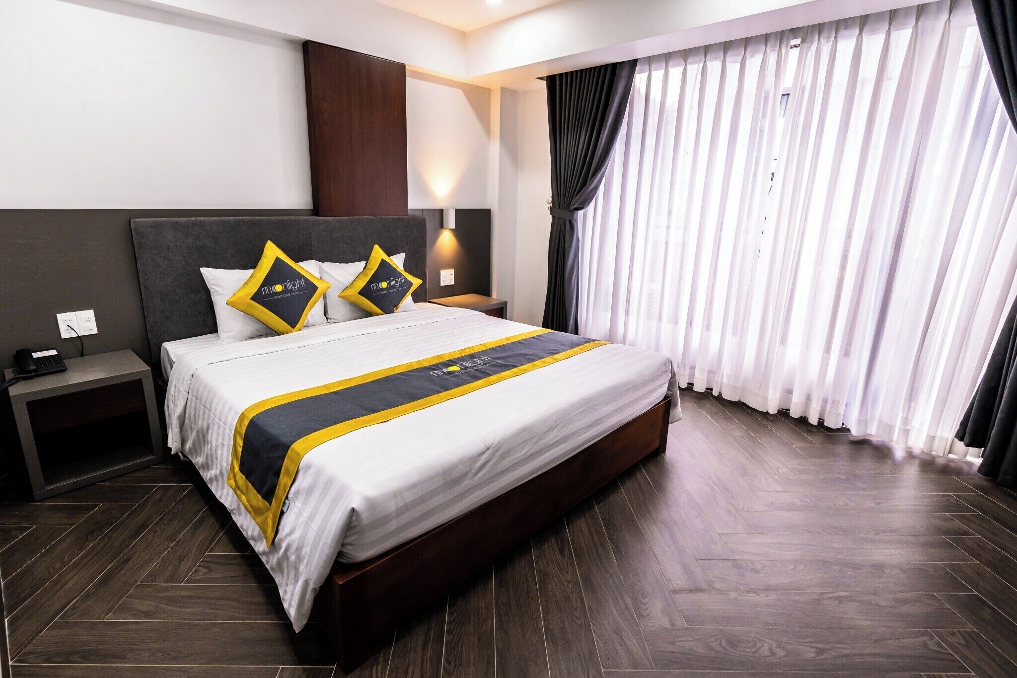 Een hotelkamer met een groot bed, twee nachtkastjes, een wandlamp en een raam met gordijnen.