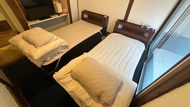 Une petite chambre, de taille modeste, comprenant deux lits simples, chacun étant équipé d’un oreiller et d’une table de chevet.