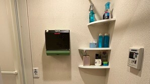 Une petite salle de bain équipée d’un porte-serviettes, d’une étagère pour les articles de toilette, d’un thermostat et d’un panier à linge.