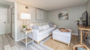 A cozy living room with a white sofa, a small side table, a wooden side table, a wicker chair, and a painting on the wall. - Camille Cottage ~ Ideal for Short-Term Stays or Traveling Professionals (Columbus)