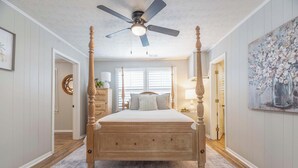 A four-poster bed with a wooden finish, a ceiling fan, and a large window with blinds. - Camille Cottage ~ Ideal for Short-Term Stays or Traveling Professionals (Columbus)