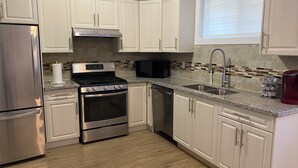 A modern kitchen with white cabinets, stainless steel appliances, a tiled backsplash, and a window with blinds. - Spacious 3-bedroom Suite in fabulous Surrey Wi-Fi, EV Charging, Basketball Court (Surrey)
