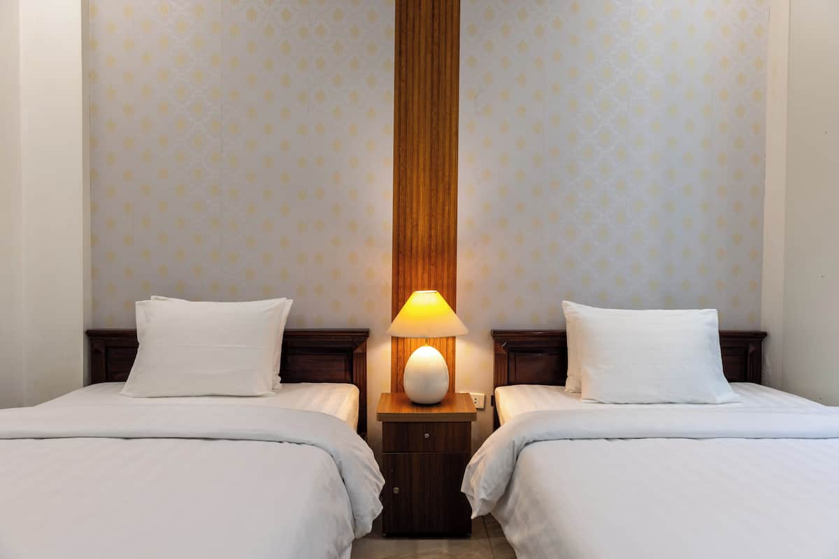 Une chambre d’hôtel avec deux lits, une table de chevet avec une lampe et un papier peint à motifs.
