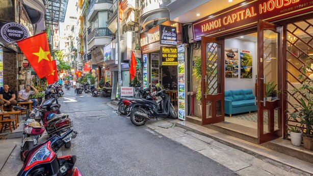 Une rue où se trouve un hôtel appelé « HANOI CAPITAL HOUSE » et un service de location de motos.