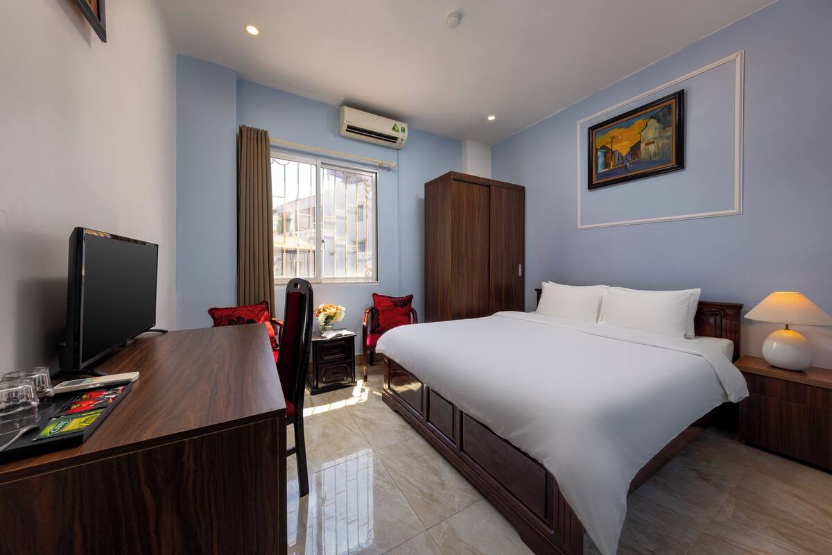 Une chambre d’hôtel avec un lit, un bureau avec une télévision, une chaise, une fenêtre et un tableau au mur.