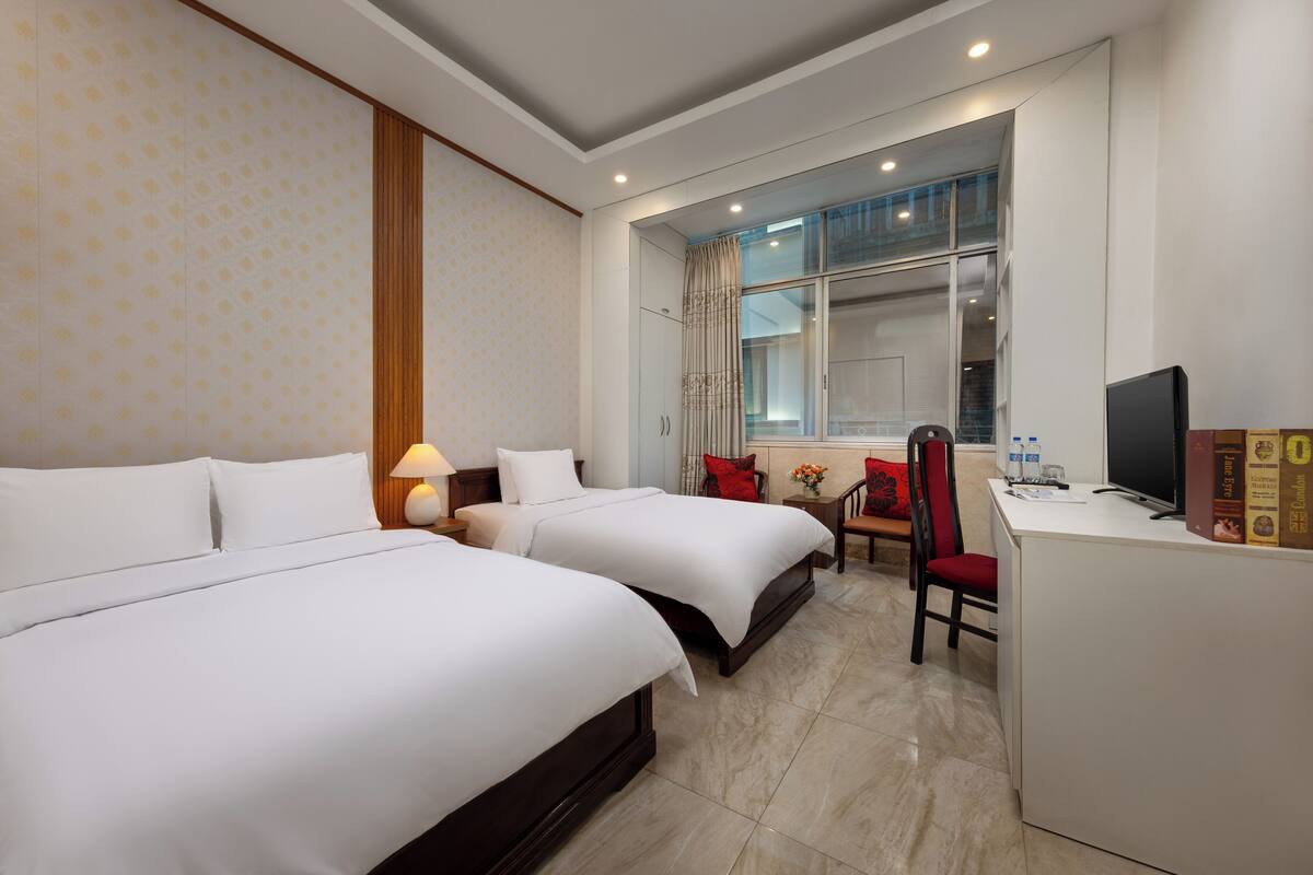 Une chambre d’hôtel avec deux lits, un bureau, une chaise, une télévision et une fenêtre donnant sur un beau paysage.