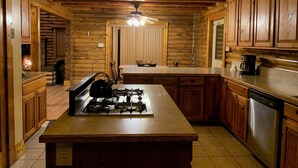 A rustic kitchen with wooden cabinets, a central island with a stove, and a ceiling light fixture.