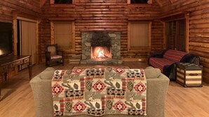 A log cabin interior with a fireplace, a sofa with a patterned blanket, and a television.