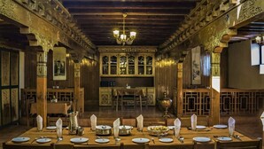 A dining area with a long table set for a meal, wooden walls, and a chandelier. - Lharimo North Cottage (Leh)