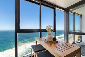 A balcony with a wooden table and chairs, overlooking a beach and ocean. - LUX Beachfront 180° Ocean View + Infinity Pool (Surfers Paradise)