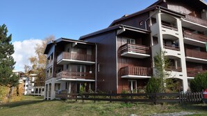 A multi-story residential building with balconies, a wooden fence, and a clear sky. - Studio near the ski station, 4 ppl, balcony (Les Deux Alpes)
