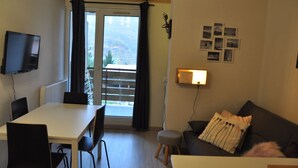 A room with a dining table, chairs, a sofa, a TV, a balcony with a view, and a wall-mounted lamp. - Studio near the ski station, 4 ppl, balcony (Les Deux Alpes)