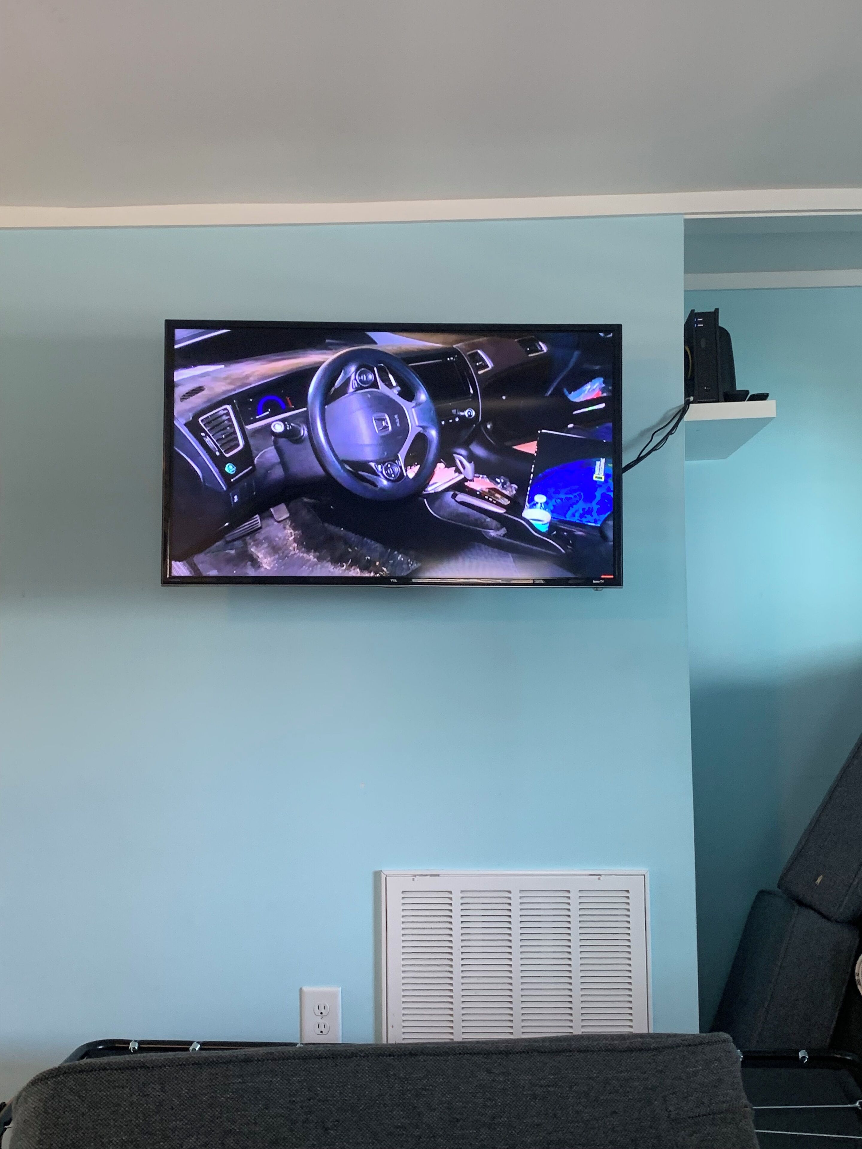 A flat-screen TV mounted on a light blue wall displaying a car's interior.
