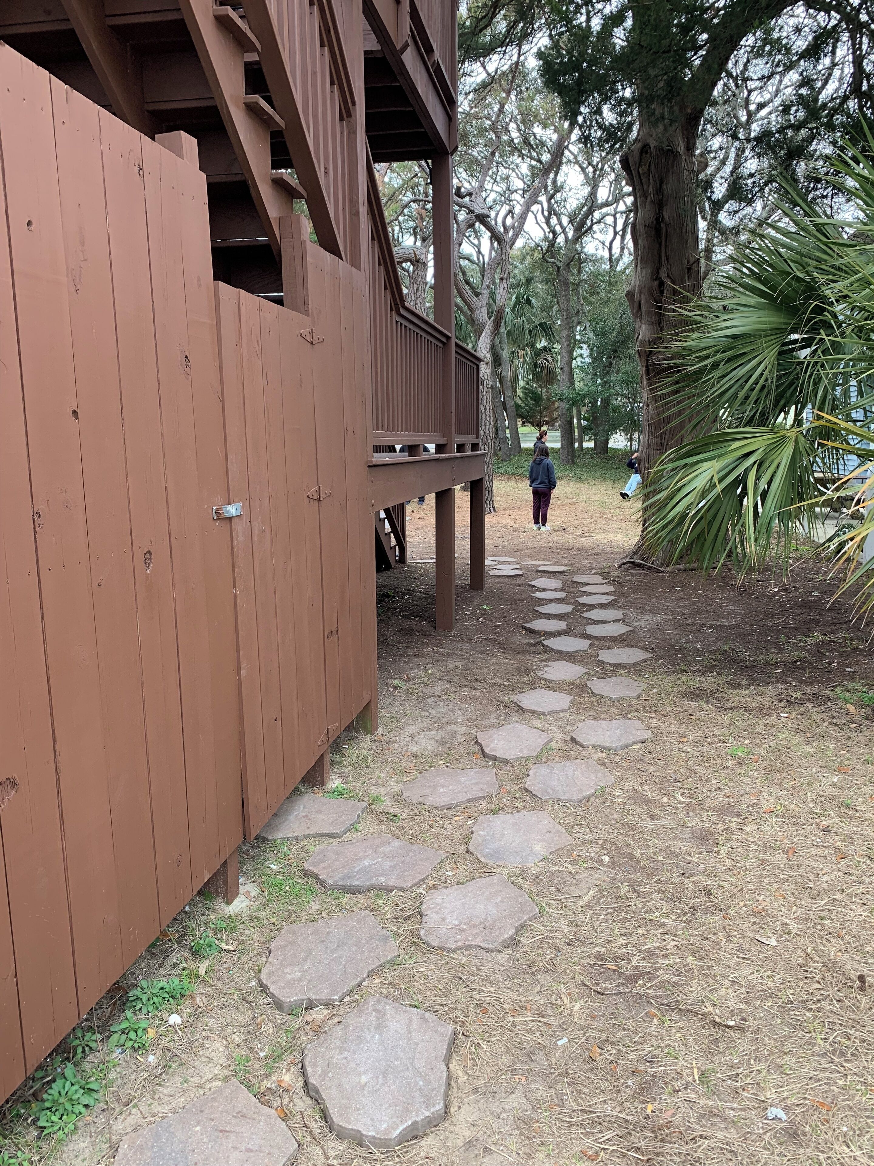 A wooden deck with a stone pathway leading to a park area.