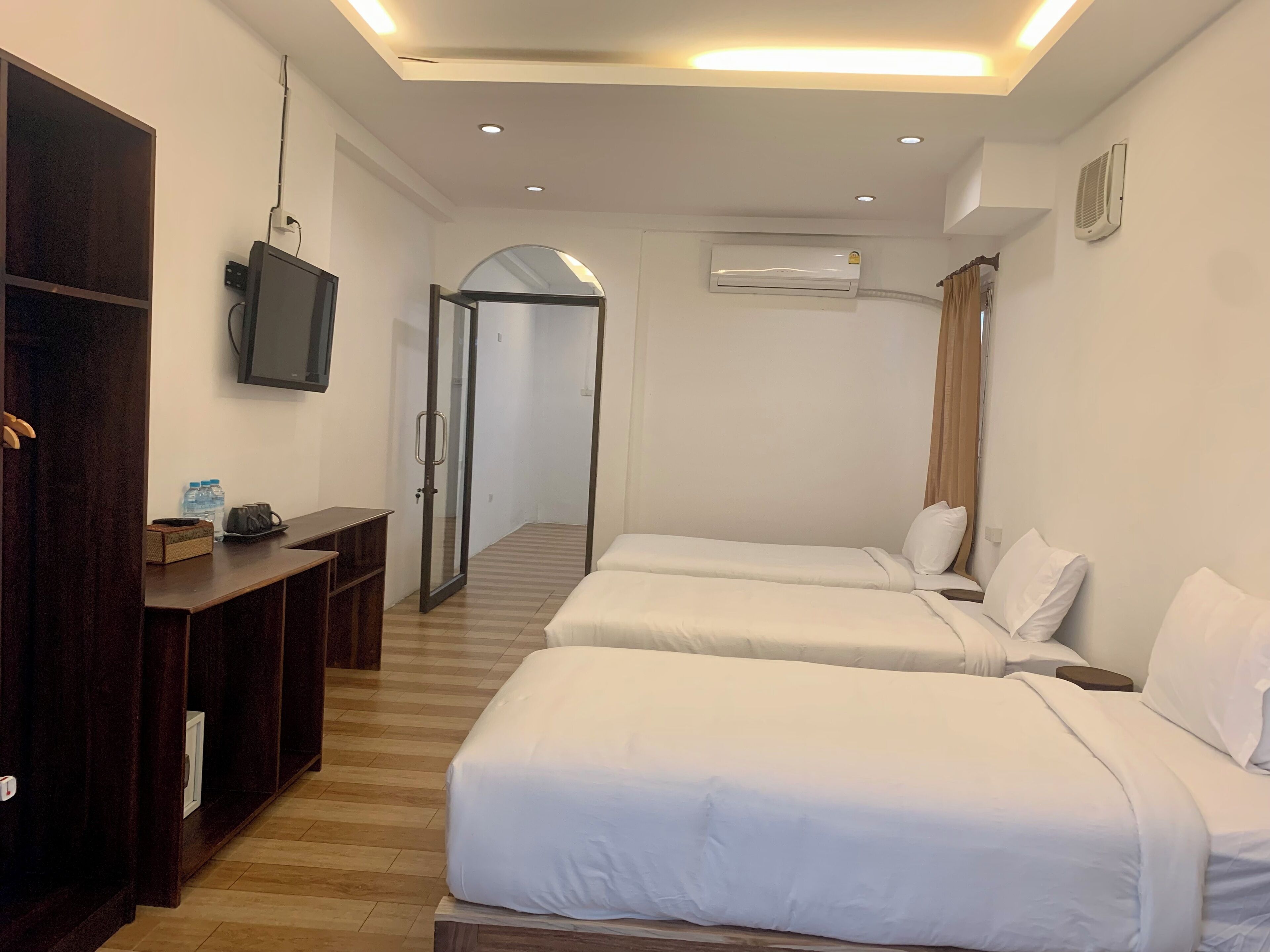 A hotel room with two beds, a desk, a TV, and an air conditioning unit.