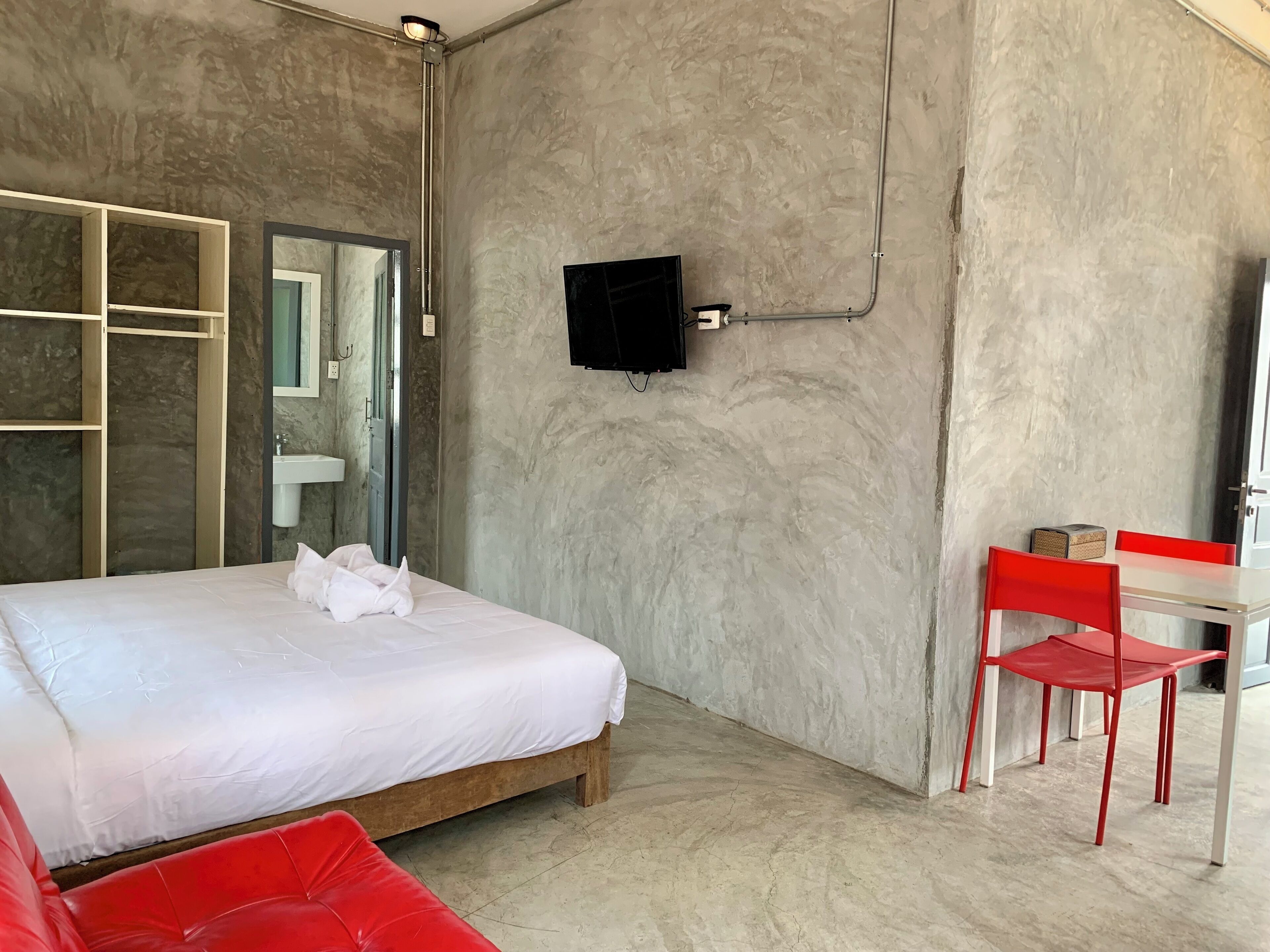 Een moderne hotelkamer met een groot bed, een houten garderobe, een tafeltje met een rode stoel en een aan de muur bevestigde televisie.
